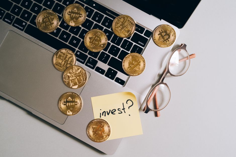 Laptop with Bitcoin coins, eyeglasses, and 'invest?' note. Ideal for finance and tech themes.