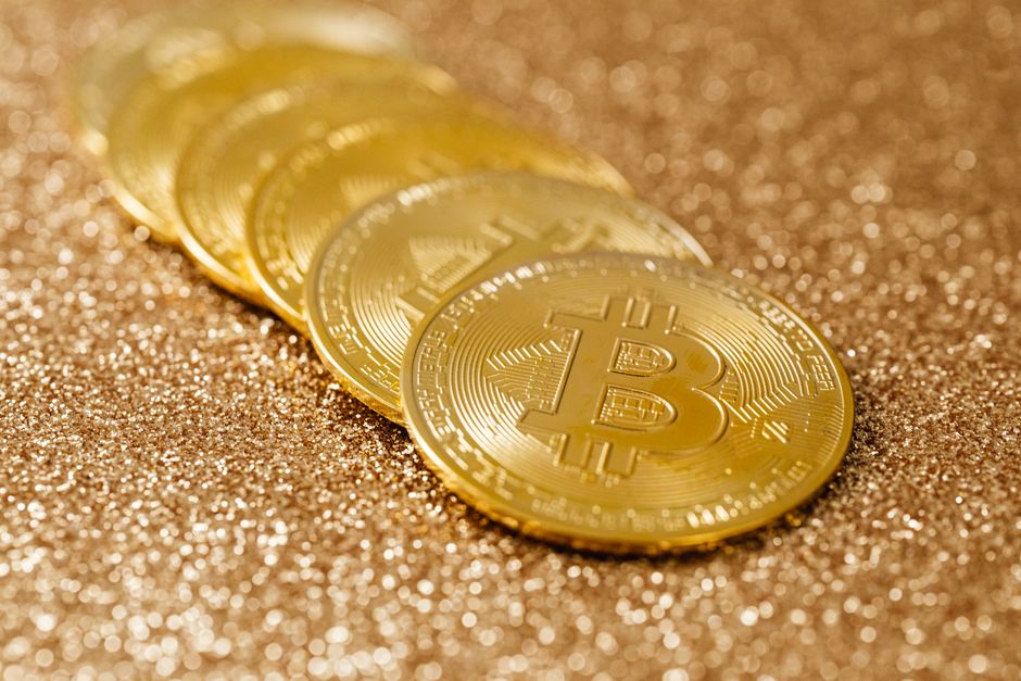 Shiny gold bitcoin coins placed on a textured glitter surface, highlighting cryptocurrency.