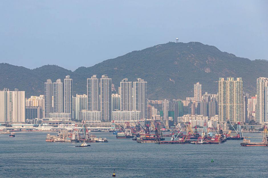 A stunning view of Hong Kong harbor with boats and towering skyscrapers set against a mountainous backdrop.