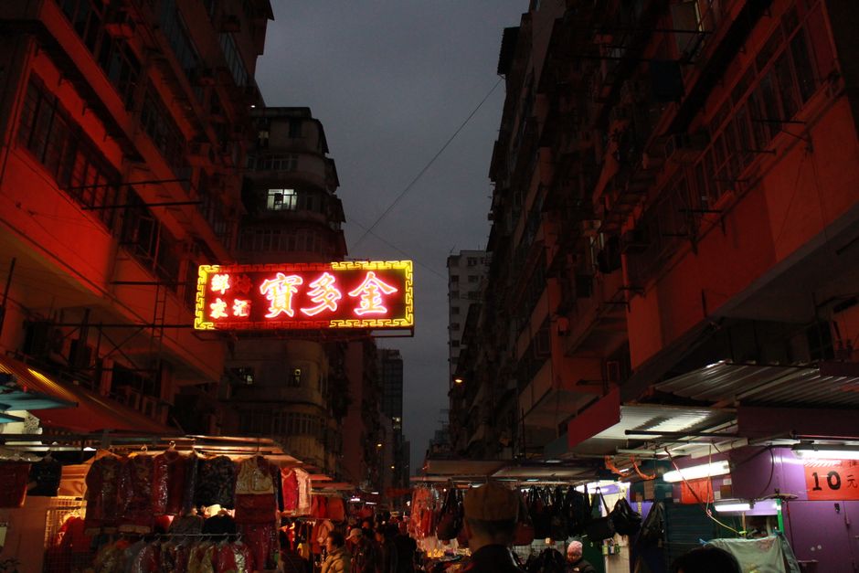A bustling urban street market illuminated by vibrant neon lights at night.