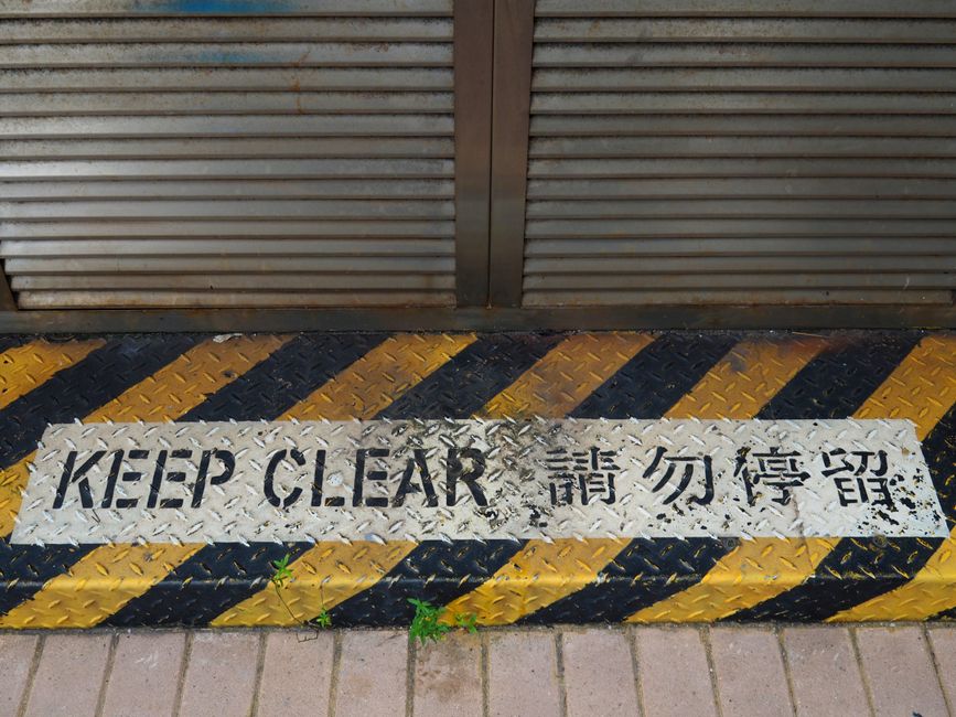 A bilingual 'Keep Clear' safety sign on a rusty metal floor in Hong Kong.