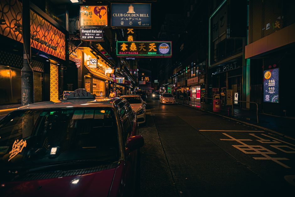 Colorful Hong Kong street at night showcasing bright neon signs and parked taxis.